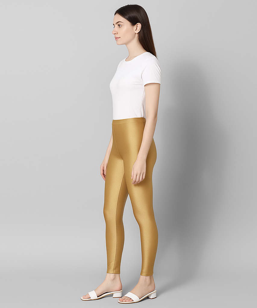 Woman wearing gold leggings and a white top on a gray background
