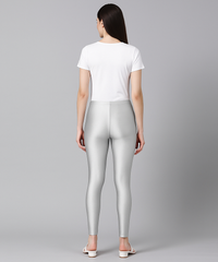 Woman wearing silver leggings and a white t-shirt on a gray background