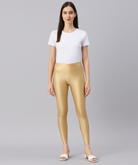 Woman wearing gold leggings and a white top on a gray background